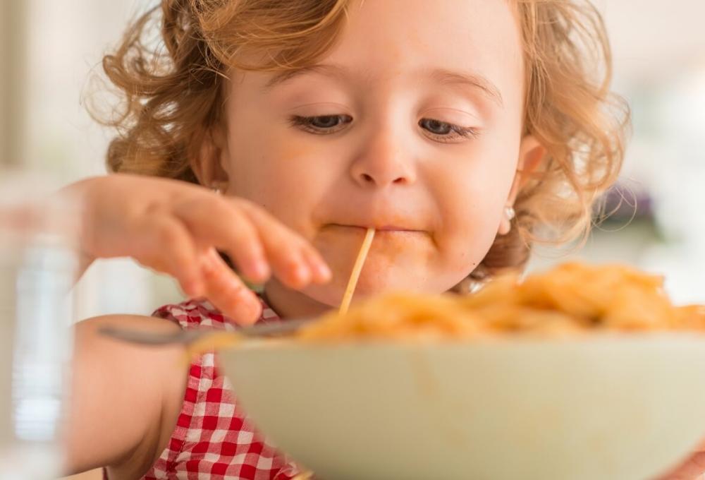 Child eagerly eats spaghetti with joy.