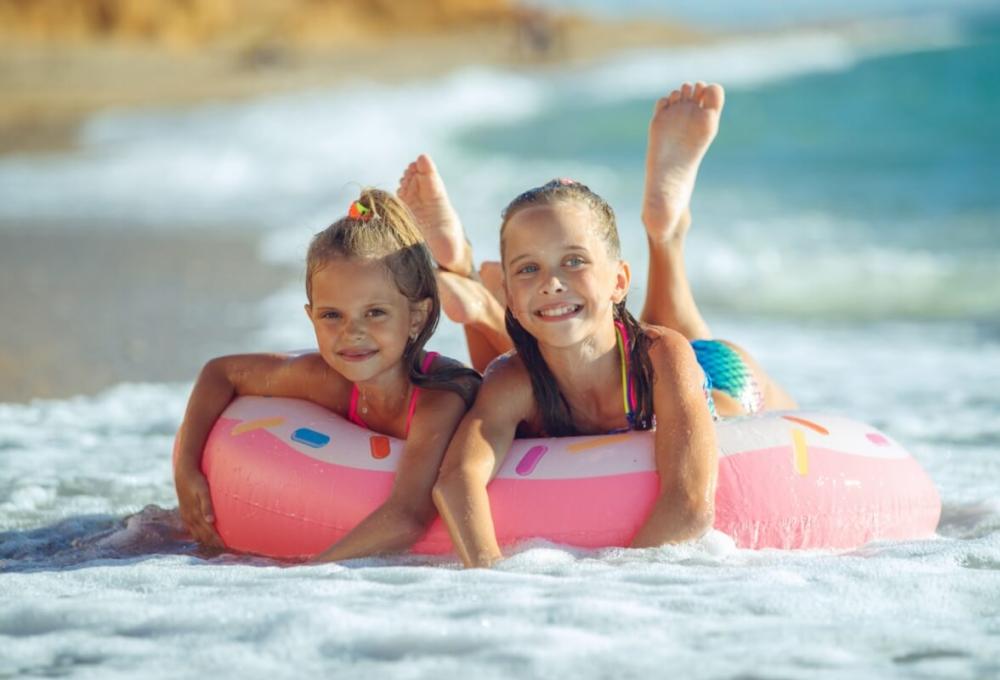 Two smiling girls on a pink float at the beach.