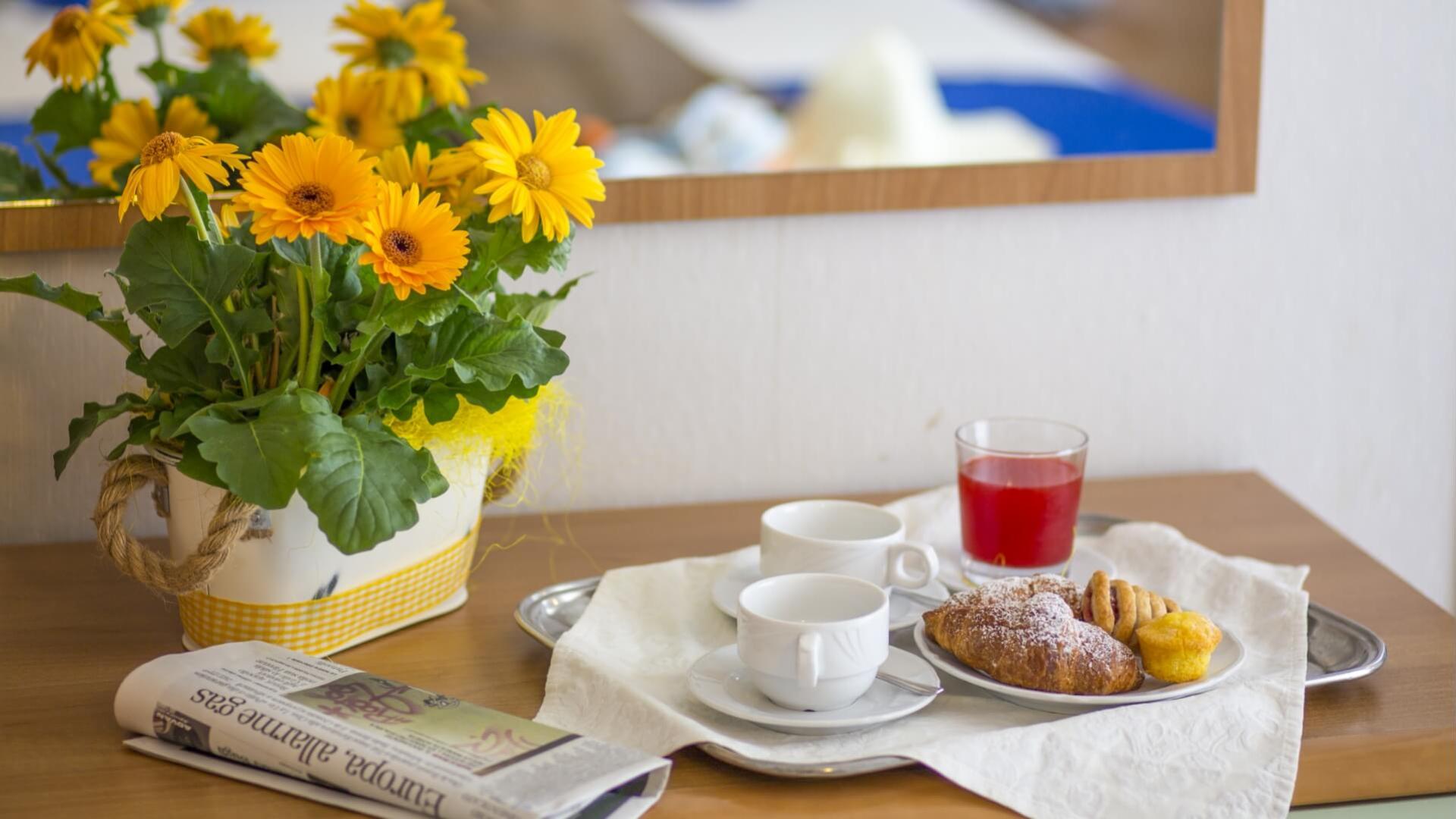 Frühstück mit Blumen, Croissant und rotem Saft auf einem Tablett.