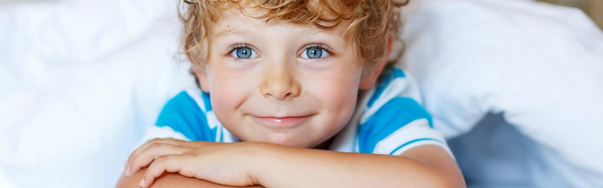 Smiling child with blue eyes under a white blanket.