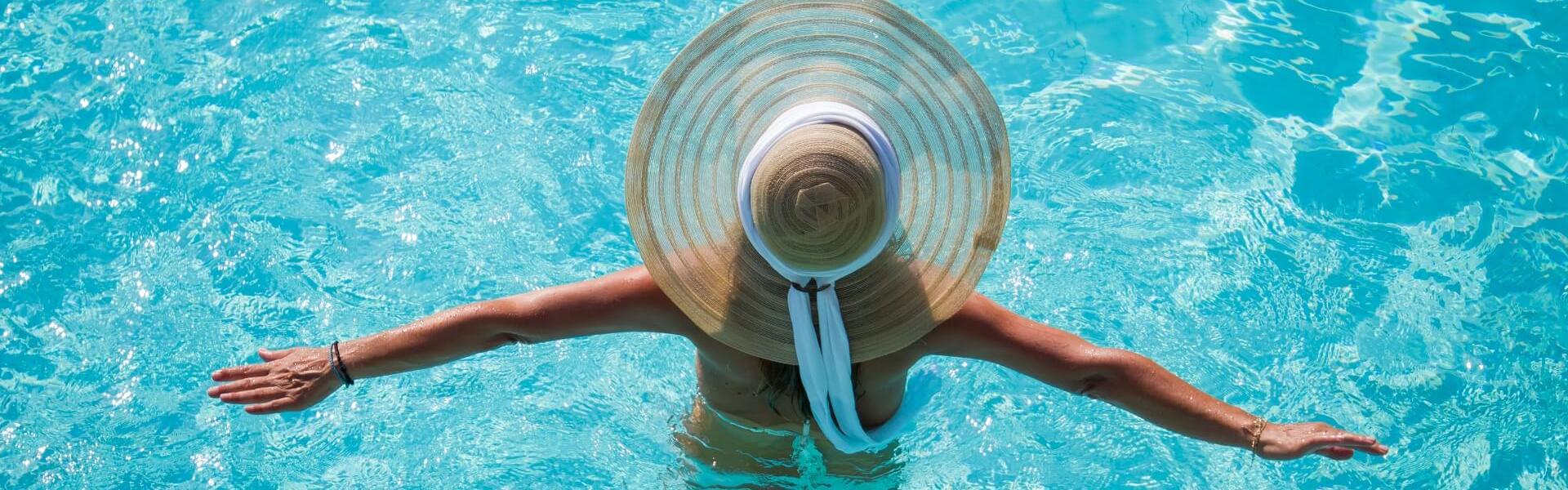 Person with hat in pool, crystal clear water.