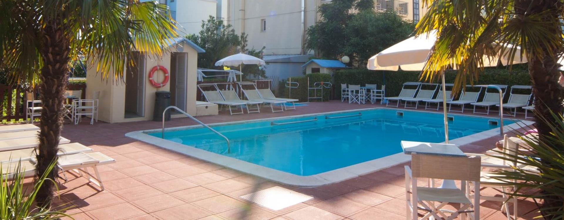 Outdoor pool with loungers and umbrellas, surrounded by palm trees.