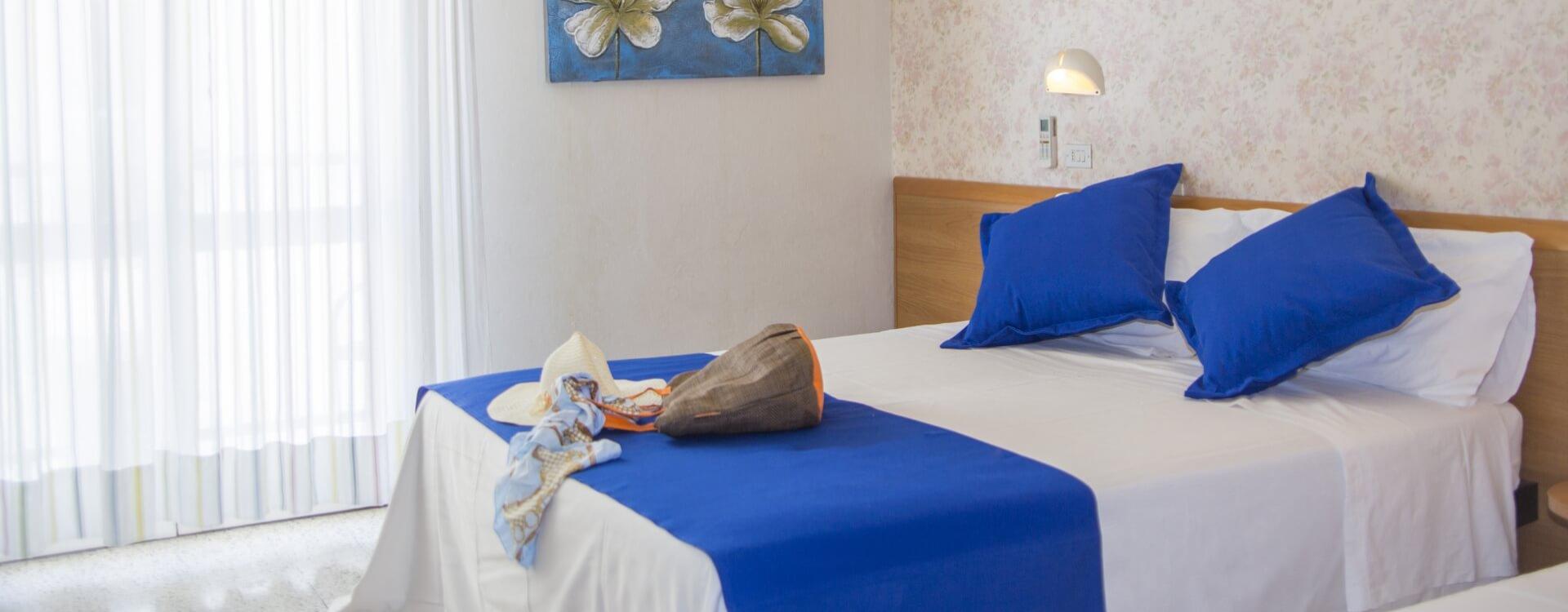 Room with double bed, blue pillows, and floral decorations.