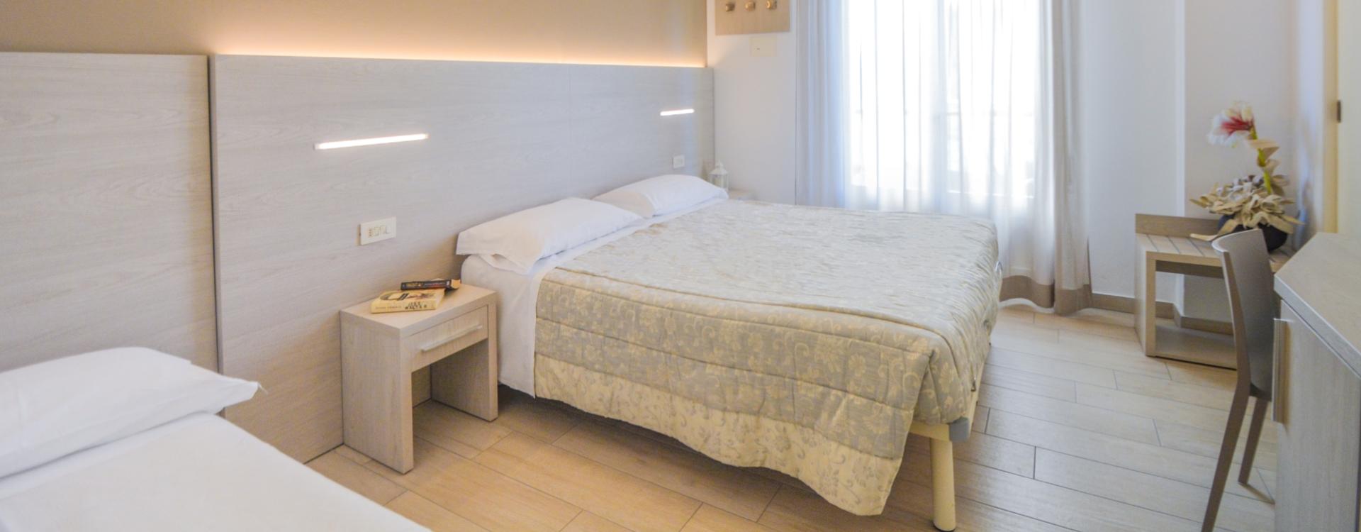 Camera luminosa con letto matrimoniale, arredamento moderno e finestra con tende.